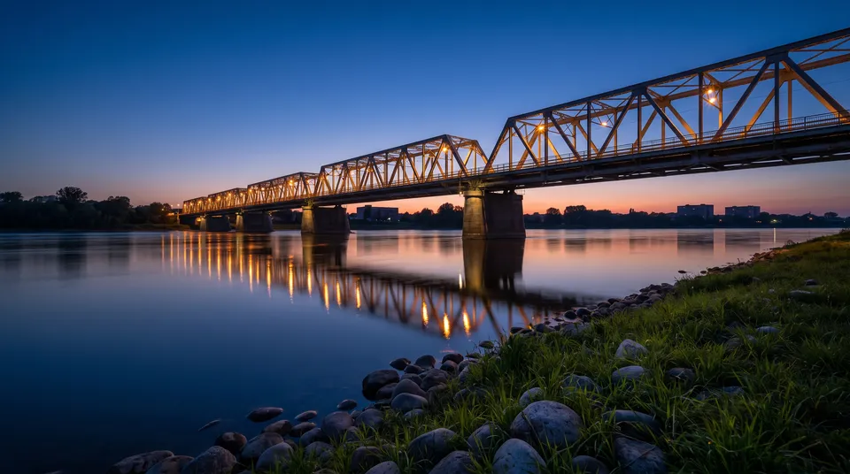 Generated scene: a long steel truss bridge over a wide river at blue hour, its lights reflected in the water.